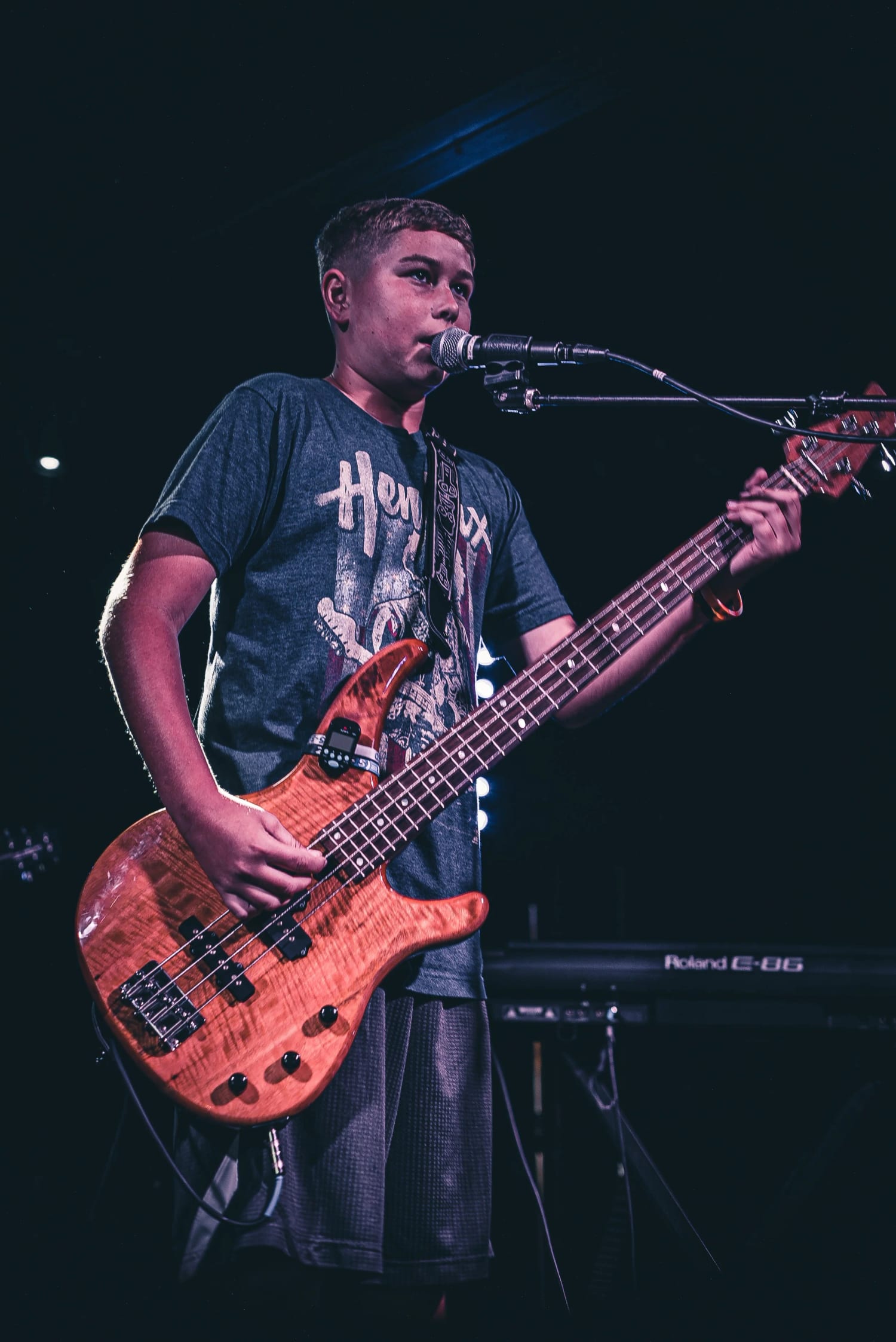 A student at the microphone playing a natural-finish electric bass
