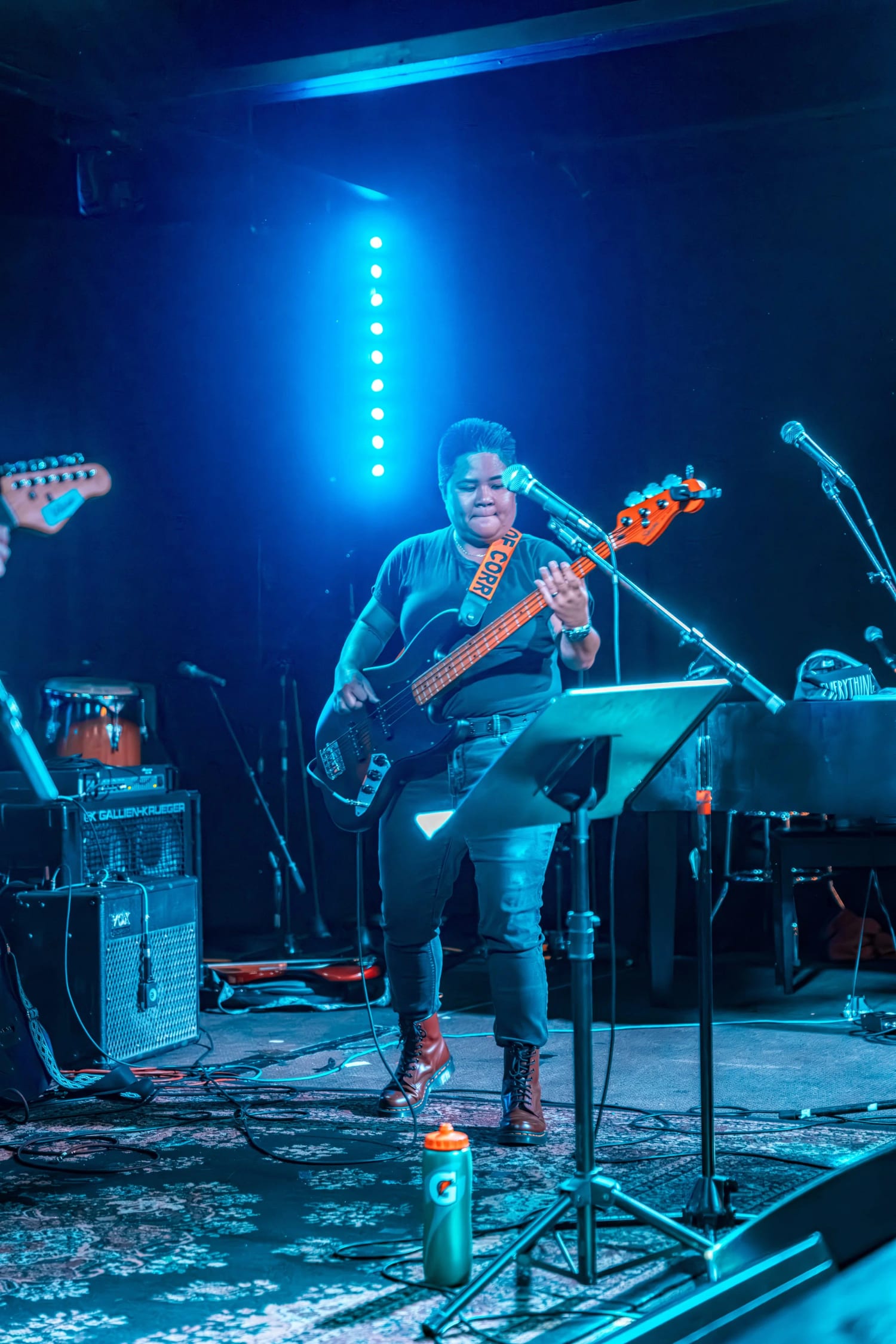 A student playing bass and singing under blue stage lighting