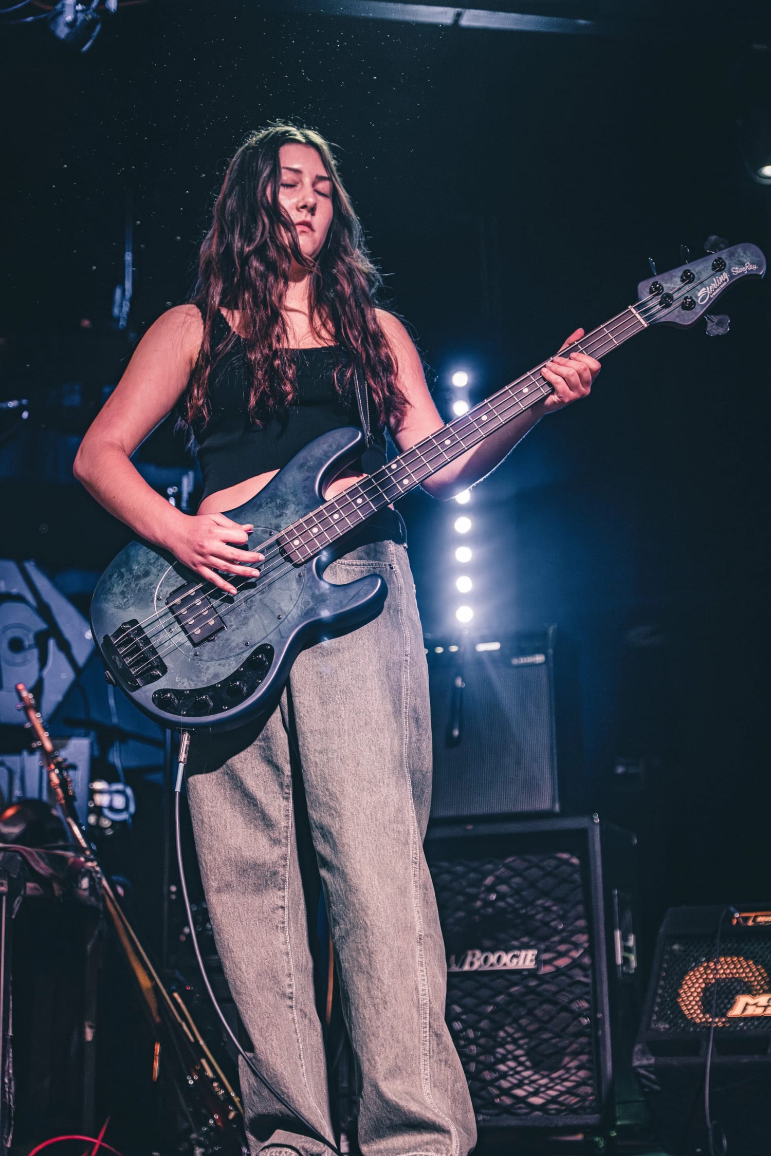 A student playing bass, lit from behind by the stage light bars