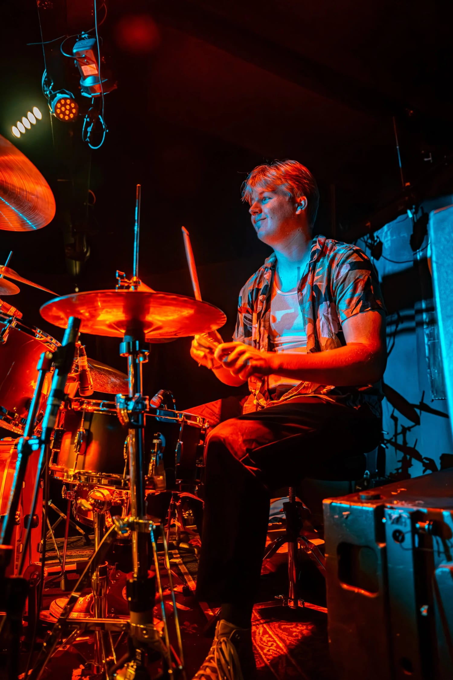A student drummer mid-fill under amber stage light