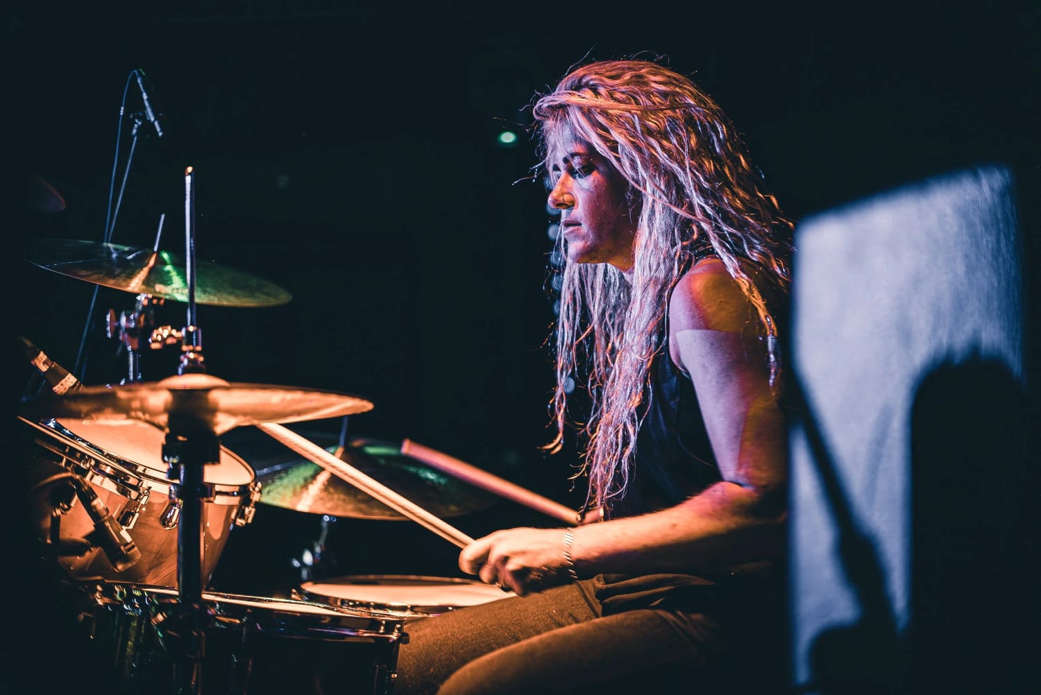 A student drummer with hair flying, gold cymbals catching the stage light