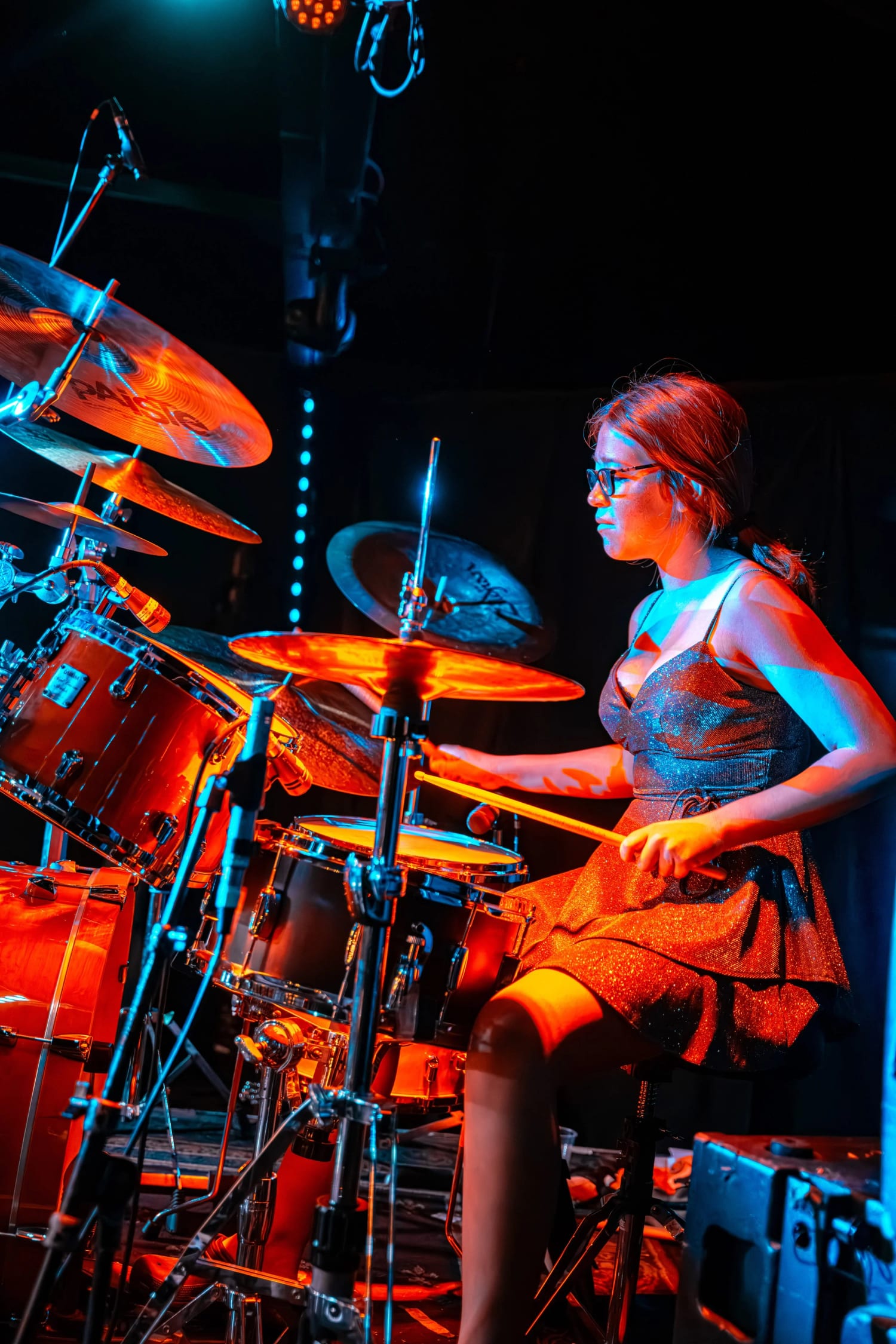 A Let There Be Rock School student playing a full drum kit under red stage wash