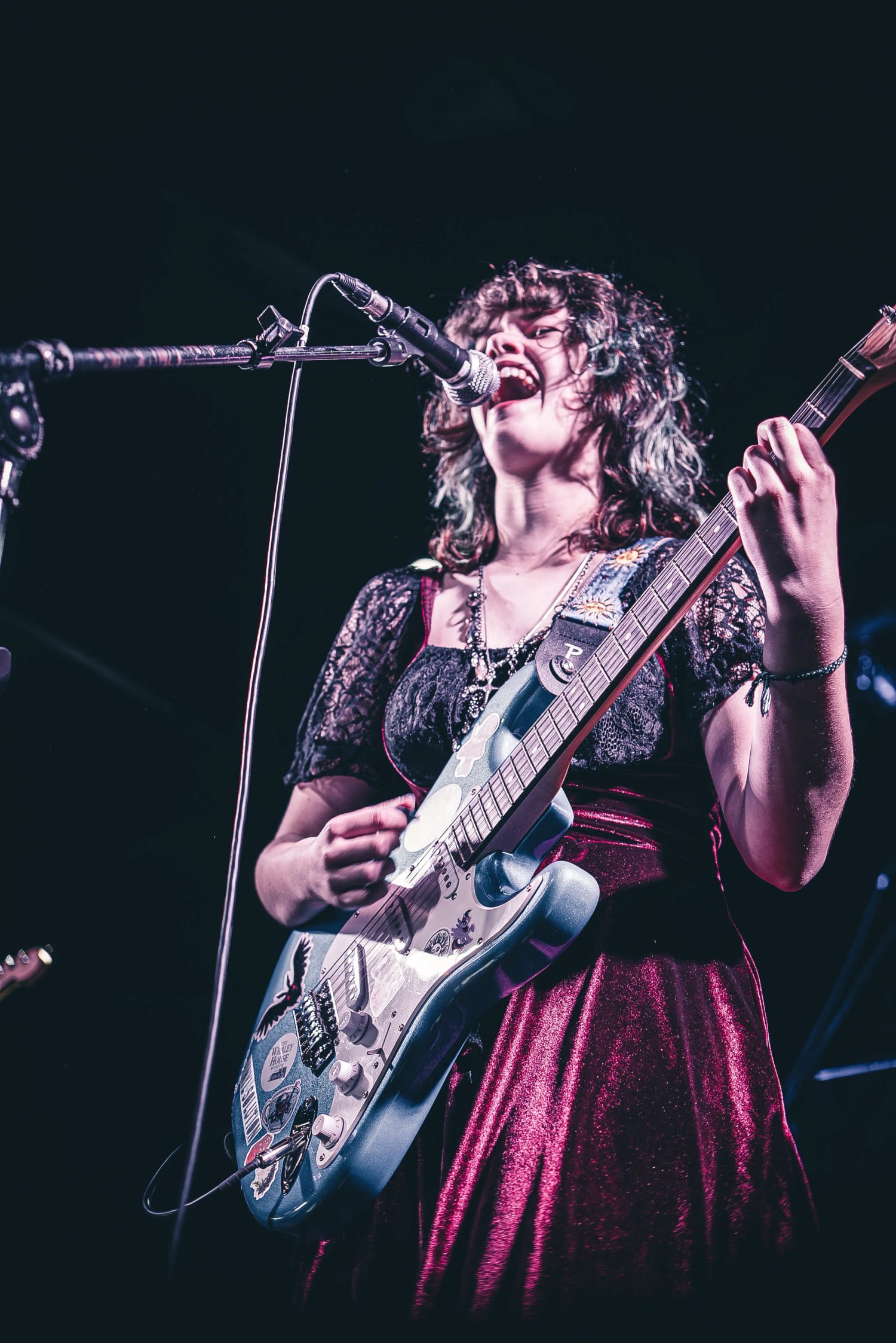 A Let There Be Rock School student singing hard into the microphone while playing electric guitar on stage