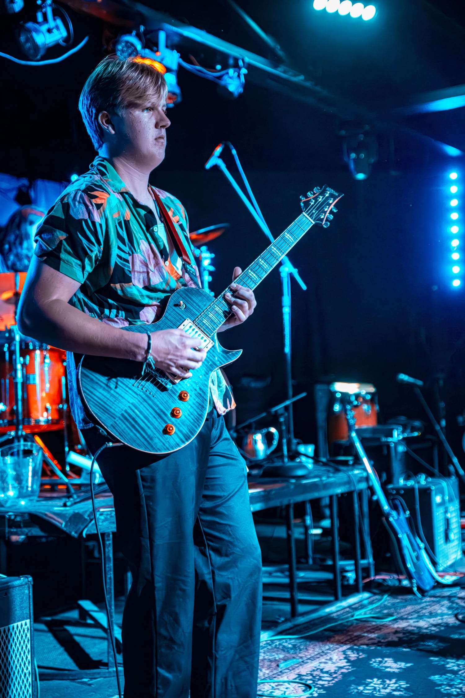 A student playing a blue flame-top electric guitar under teal stage lights