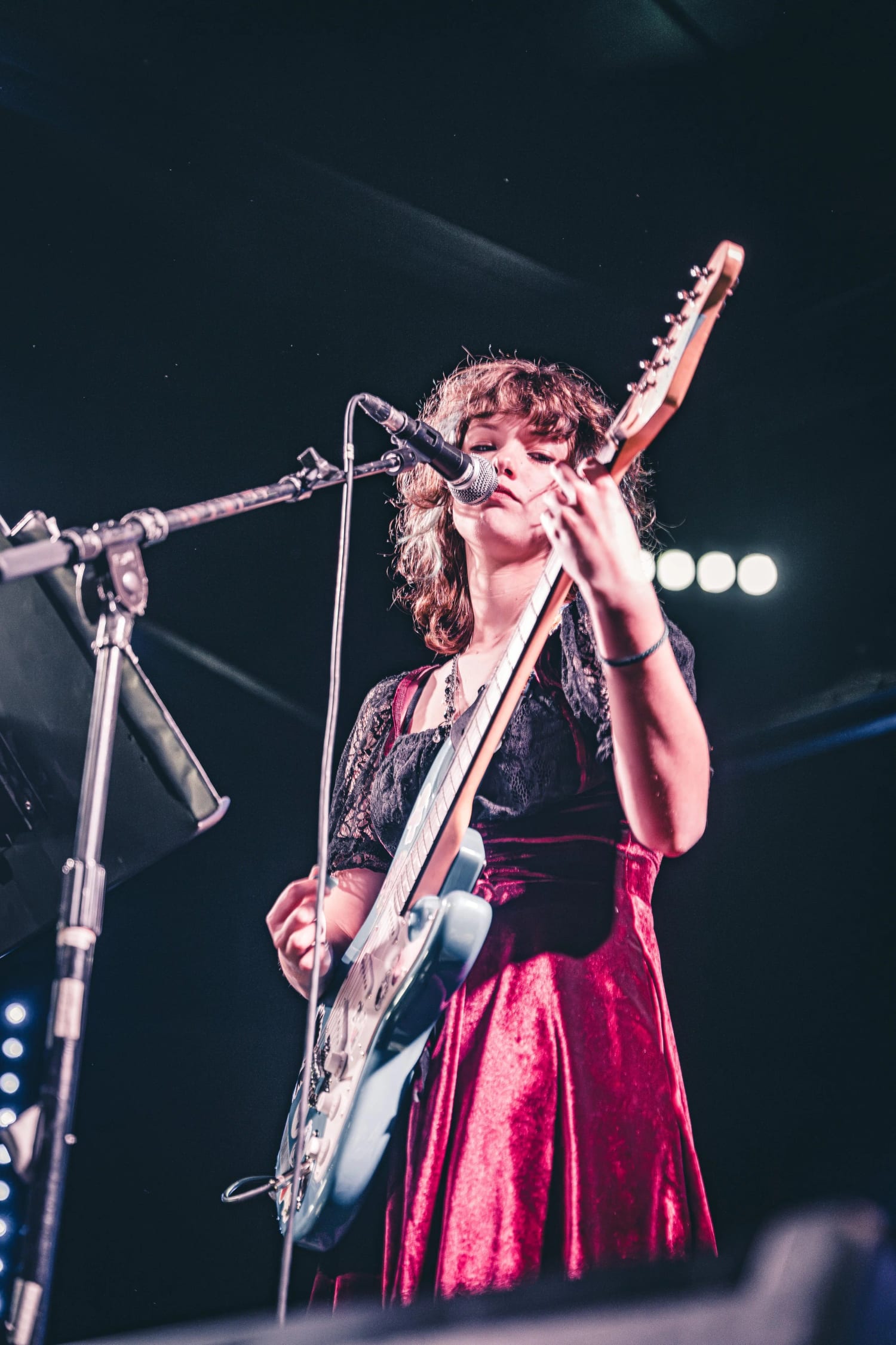 A student singing into the microphone while playing electric guitar on stage