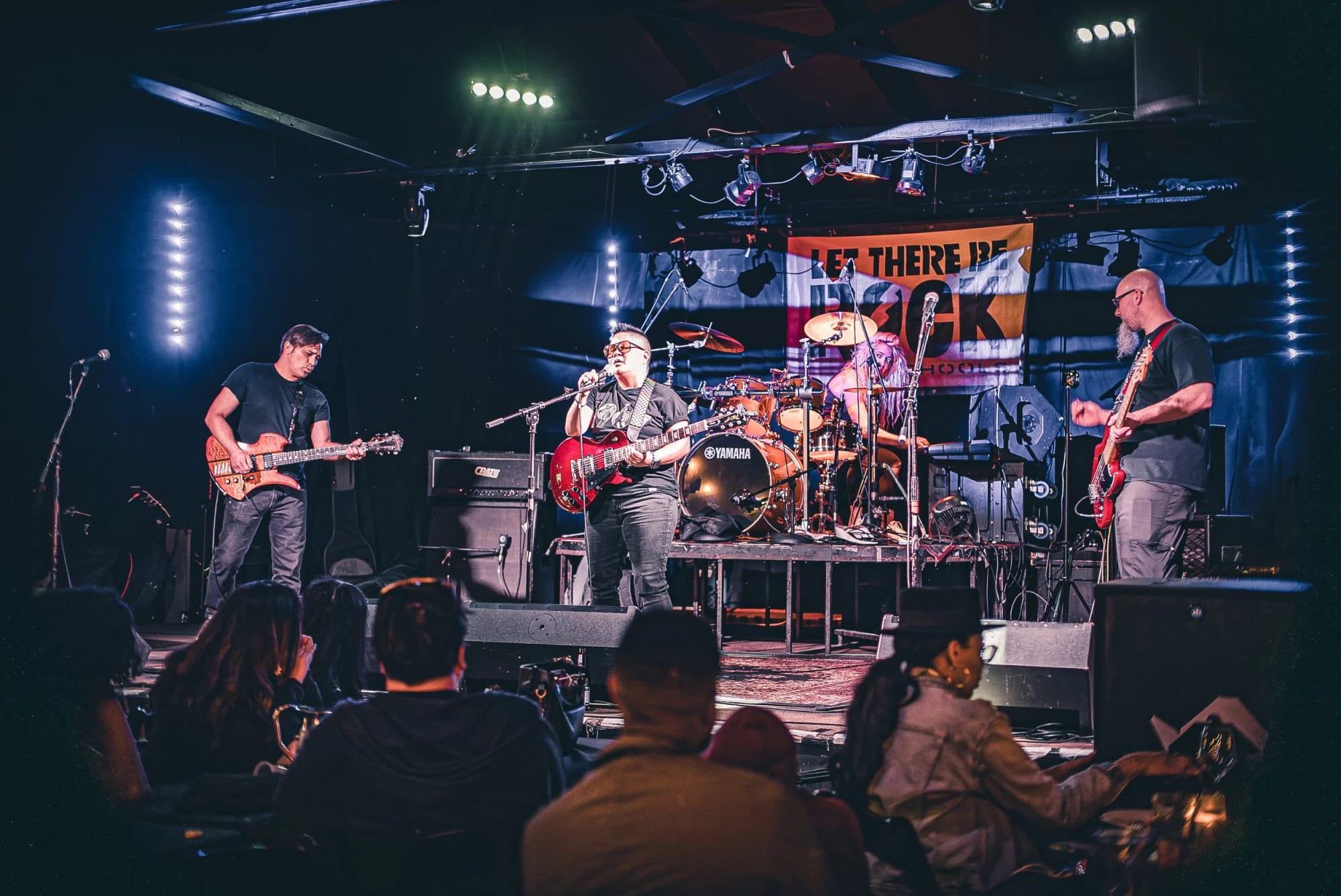 Wide view of a Let There Be Rock School student band performing to a seated audience in a Long Beach club
