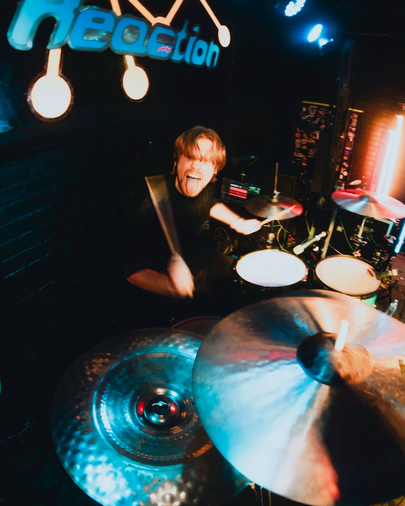 Jackson Shearer playing drums on stage under blue light, sticks raised