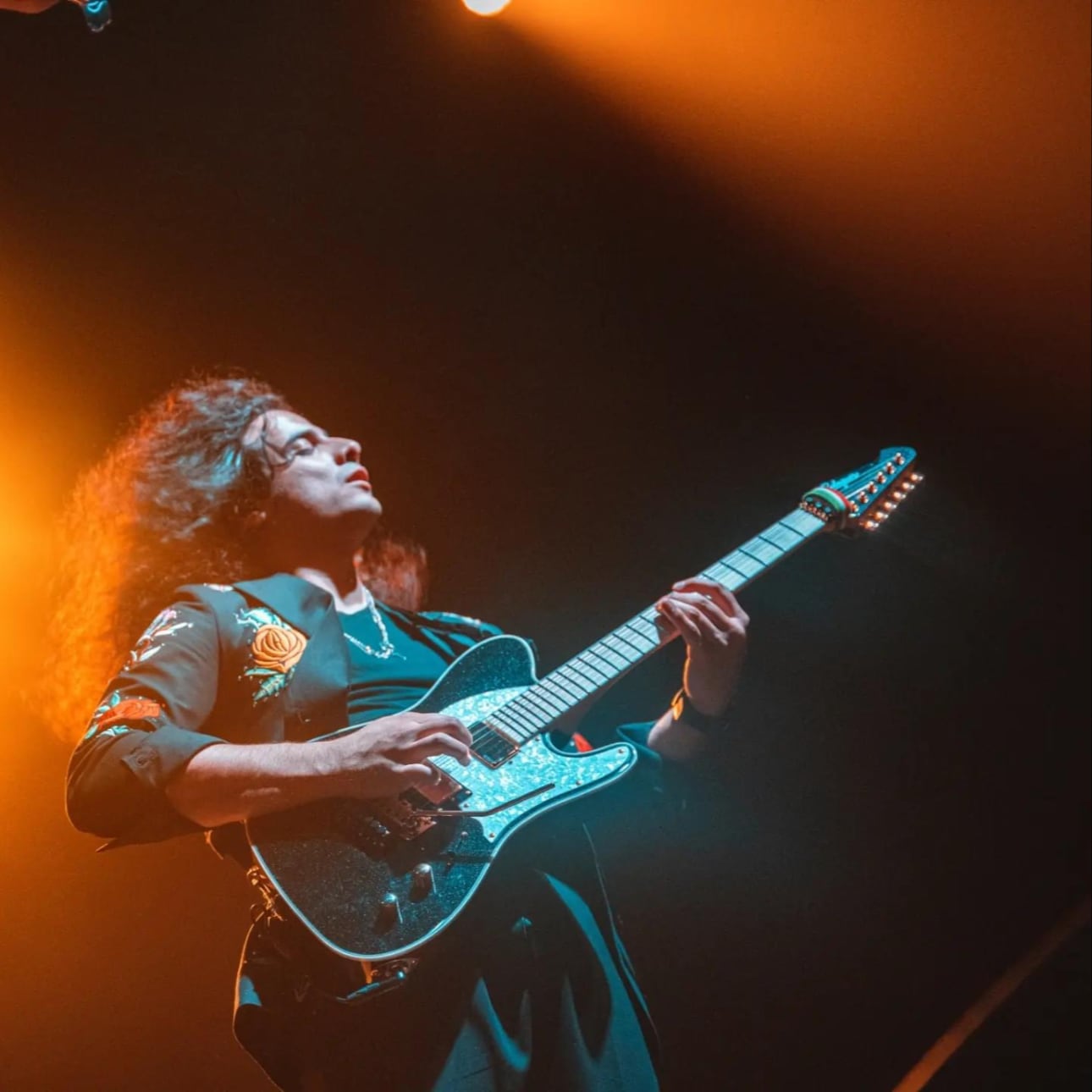 Jacob Ortiz playing electric guitar on stage under orange and teal lighting